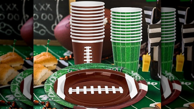 Decorative football party paper plates with themed cups and other decor behind them on a table.