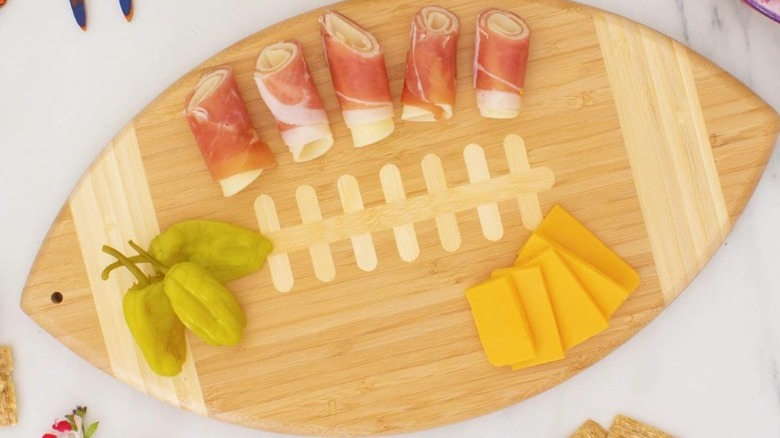 A football-shaped cutting board and charcuterie board with cheese, meat, and peppers on it.