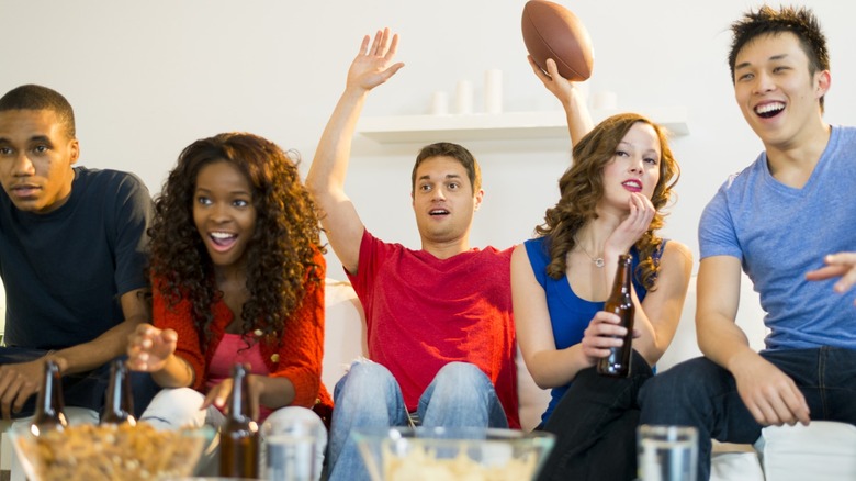 Five people sitting on a couch with bowls of snacks in front of them.