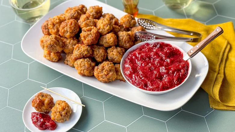 Sausage balls served on a white rectangular plate with a bowl of cranberry sauce