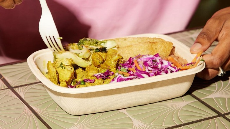 A person holding a takeout container of Caribbean food at Aventura Mall