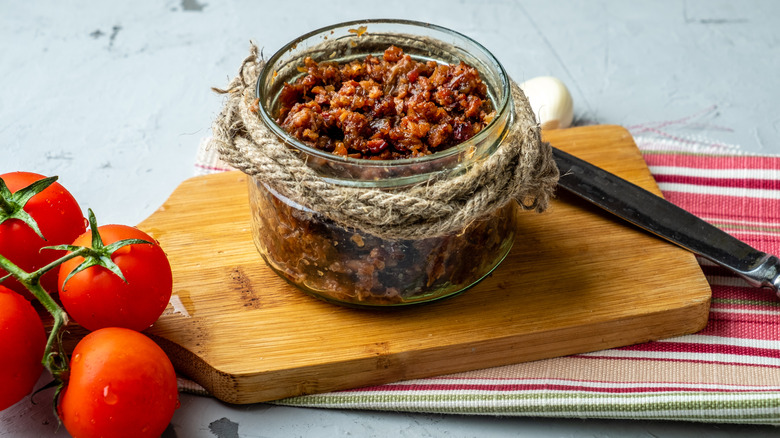 A jar of bacon jam on a wooden cutting board next to tomatoes