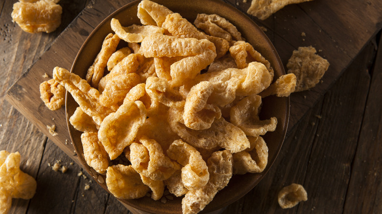 A bowl of crispy pork rinds on a wooden cutting board