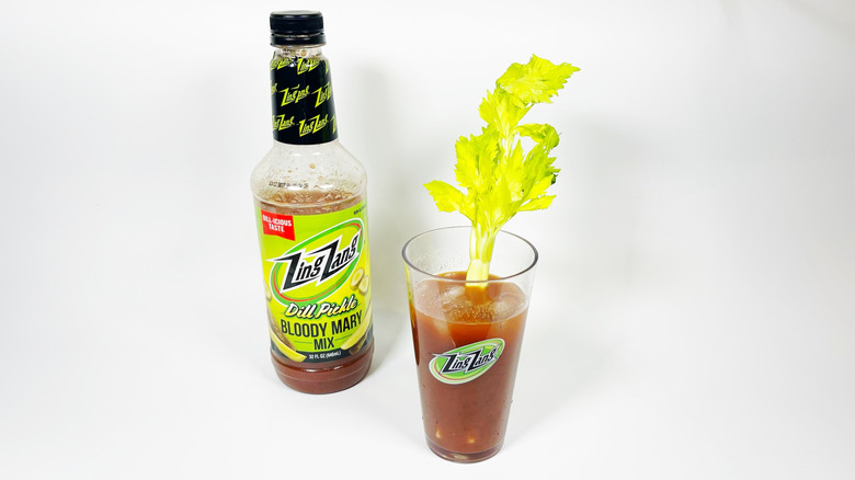 A bottle of Zing Zang dill pickle next to a glass filled with mix and garnished with celery