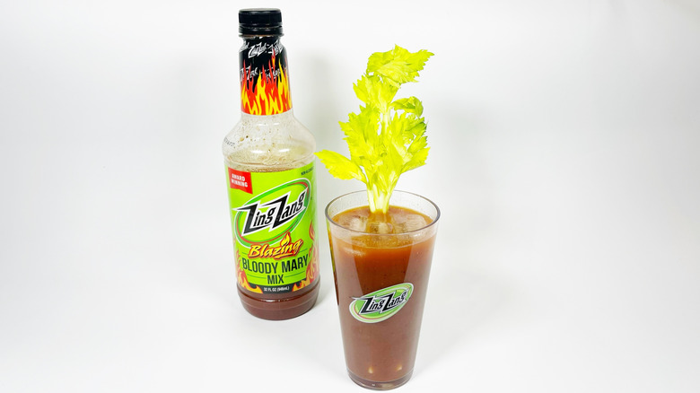 A bottle of zing zang blazing next to a glass filled with mix and garnished with celery