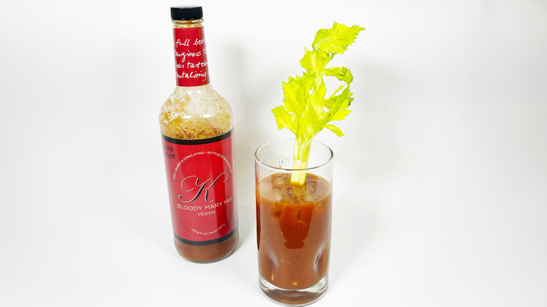 A bottle of K Bloody Mary Deep Heat next to a glass filled with mix and garnished with celery