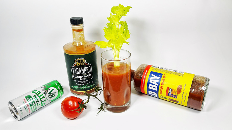 A few Bloody Mary mixes on a white background with a tomato and glass
