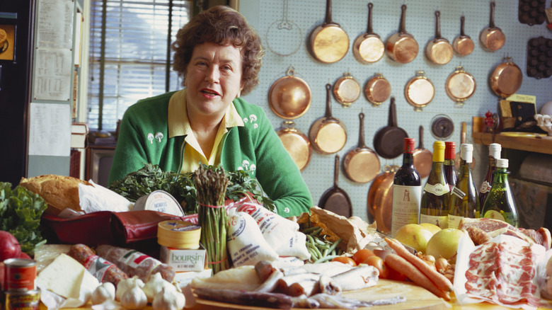 Julia Child sitting at a table covered with food in her kitchen