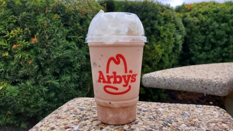 Arby's chocolate milkshake with bushes in background