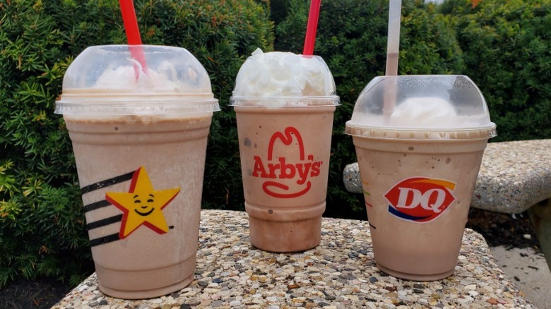 chocolate milkshakes from Hardee's, Arby's, and Dairy Queen with bushes in background