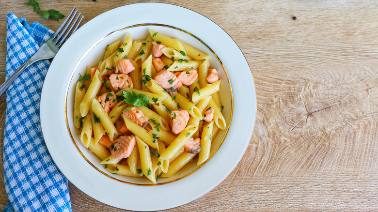 Penne pasta with salmon in a white bowl on a wooden surface