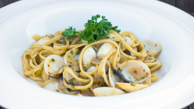 Spaghetti with clams in a white bowl with parsley on top