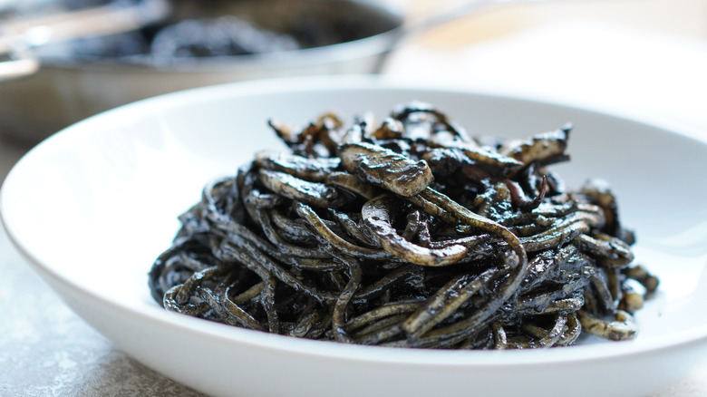 Bowl of black squid ink spaghetti, contrasted against the white surface