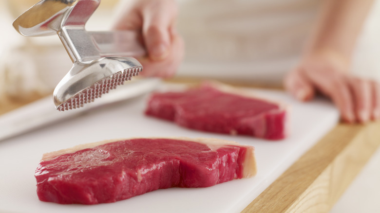 Meat mallet to tenderize raw steak on a cutting board