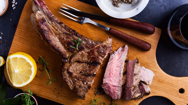Bone-in steak on a cutting board with rosemary and lemon