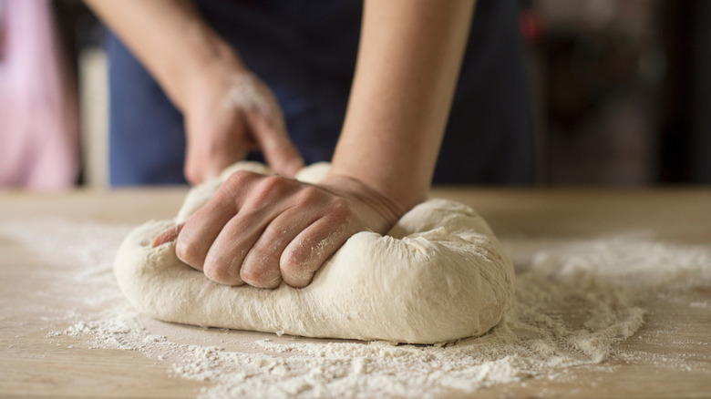 Two hands are kneading dough on a floured board.