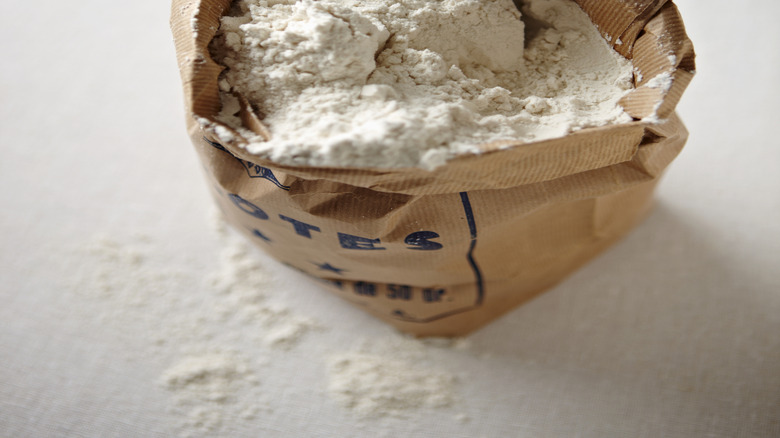 A bag of flour has a scoop in it.