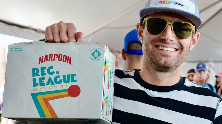 Smiling man holding up a case of Harpoon Rec. League Low-Cal Hazy IPA