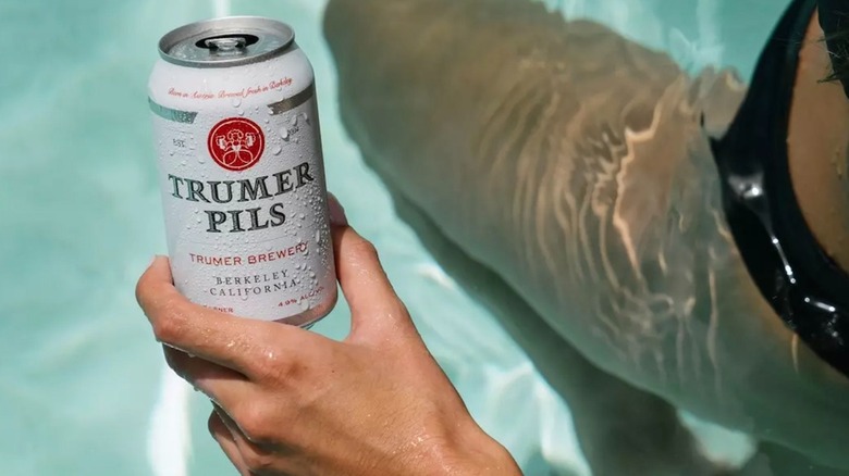 Hand holding a can of Trumer Pils in the pool