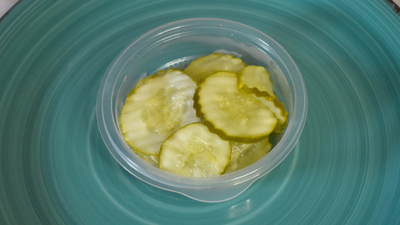 A small plastic cup of KFC pickles on a blue plate