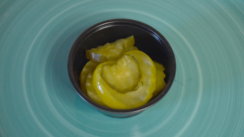 A small black plastic cup of Subway pickles on a blue plate