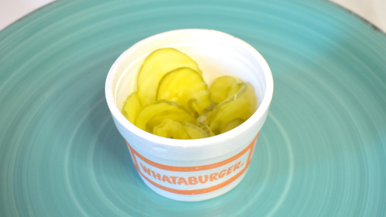 A small white takeout cup of pickles on a blue plate