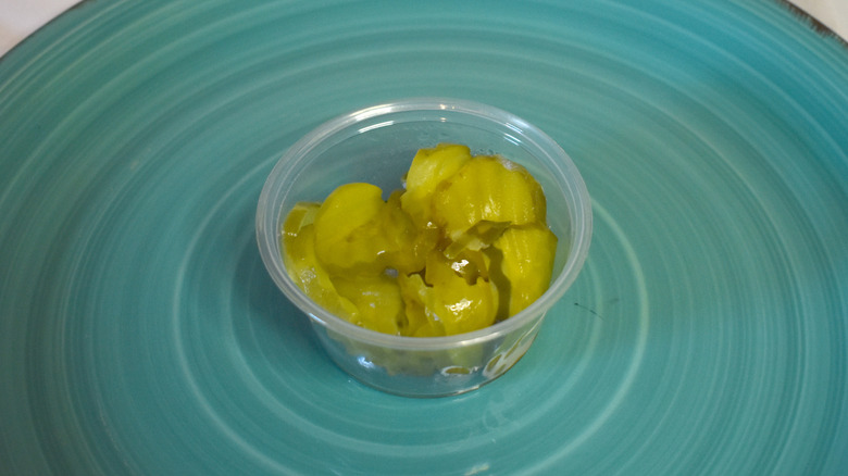 A plastic cup of pickles on a blue plate