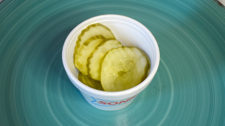 A small paper cup of Sonic pickles on a blue plate