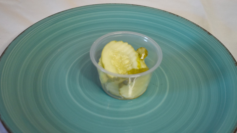 A small plastic cup of Jersey Mike's pickles on a blue plate