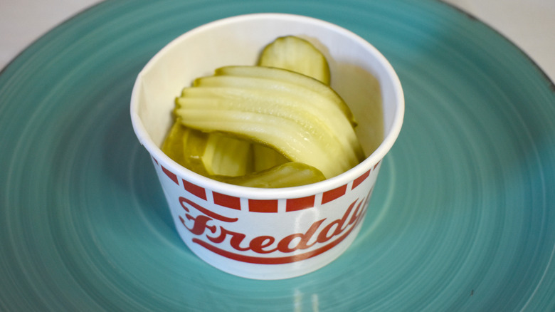 A paper cup of Freddy's pickles on a blue plate