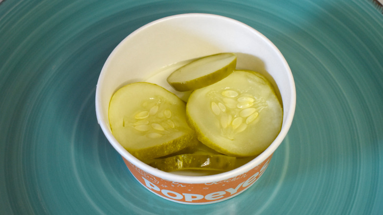 A paper cup of Popeye's pickles on a blue plate