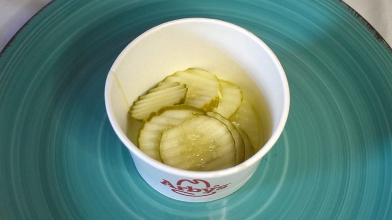 A paper cup of Arby's pickles on a blue plate