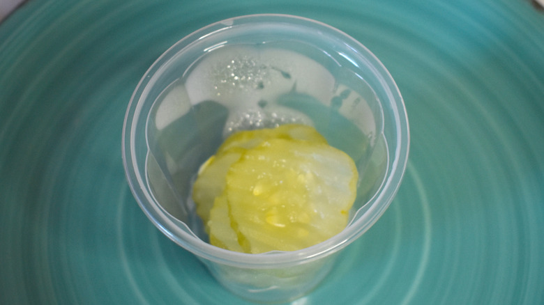 A plastic cup of Burger King pickles on a blue plate