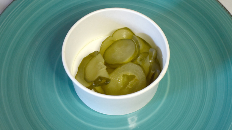 A paper cup of McDonald's pickles on a blue plate