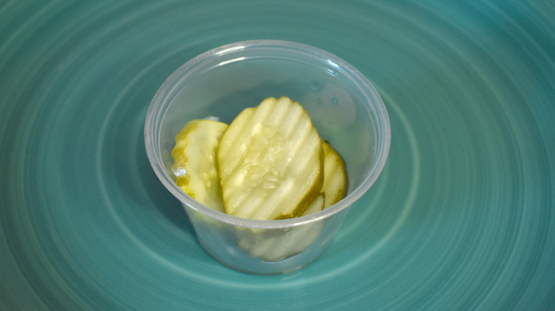 A small plastic cup of Carl's Jr. pickles on a blue plate