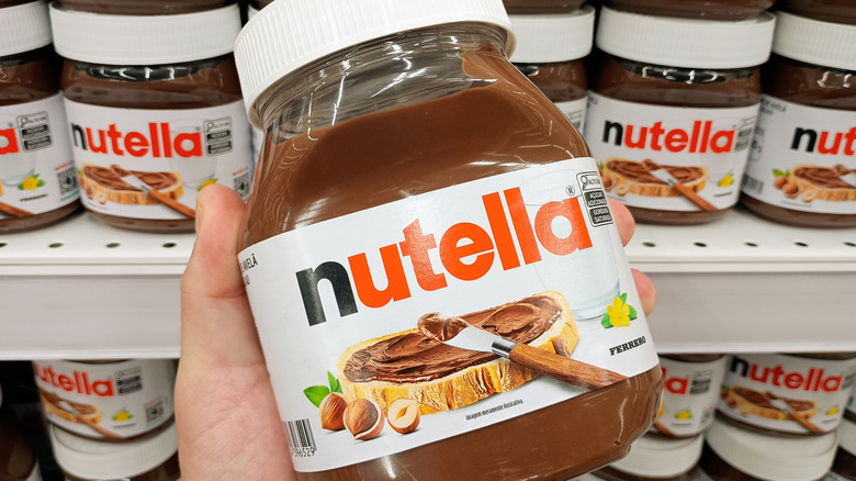 Someone holding a jar of Nutella in front of a store shelf of nutella jars