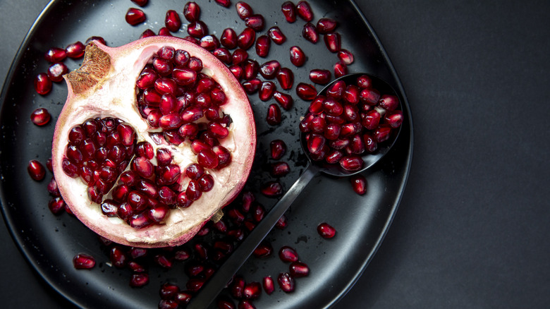 Half of a pomegranate with seeds and a spoon on a black plate