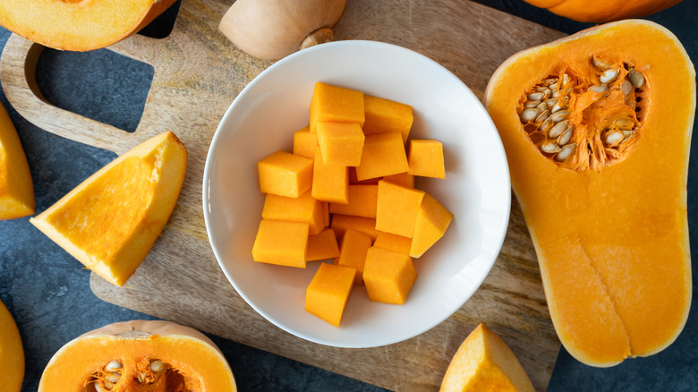Bowl of diced butternut squash surrounded by larger pieces on a cutting board