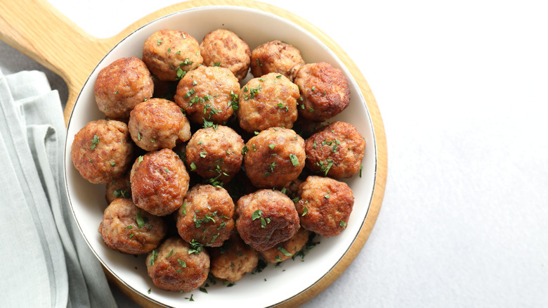 Bowl of cooked meatballs on round, wooden serving board