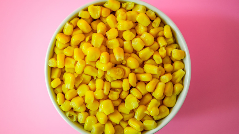 White bowl filled with sweet corn on a pink background