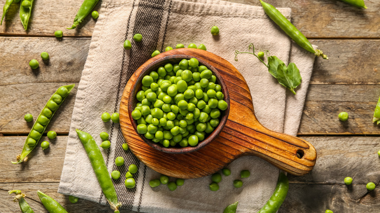 Green peas in a wooden bowl, served on a wooden cutting board
