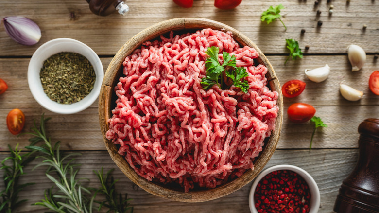 Ground beef in a wooden bowl, surrounding by spices