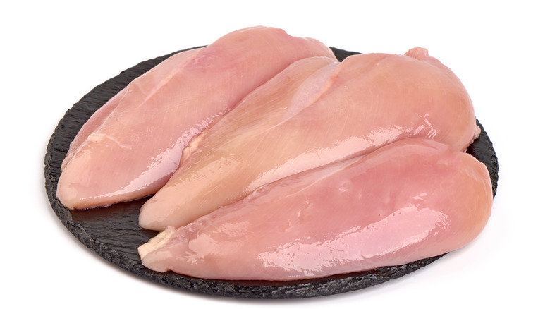 Raw chicken breasts on a black slate plate