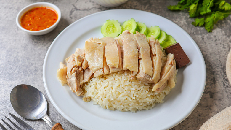 A plate of Hainanese chicken rice with cucumbers and chili sauce