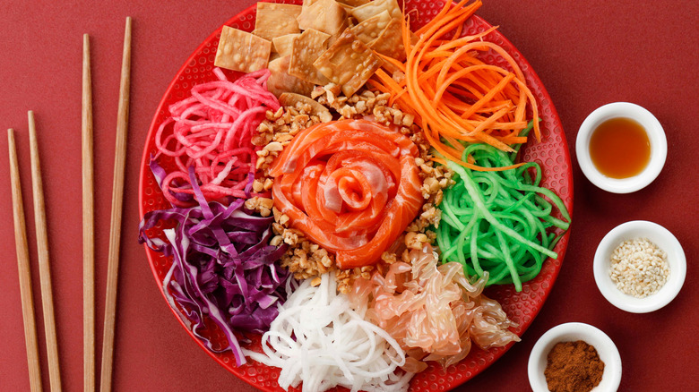 A plate of yu sheng with raw fish, julienned vegetables, and crackers