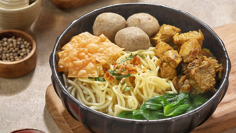 A bowl of bakso soup with meatballs, chicken, noodles, and crispy crackers