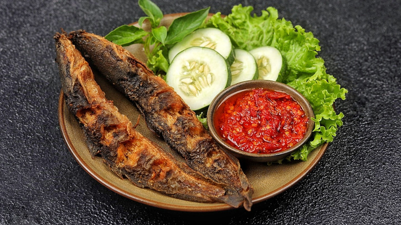 A plate of pecel lele (fried catfish) with cucumbers, lettuce, and cucumber