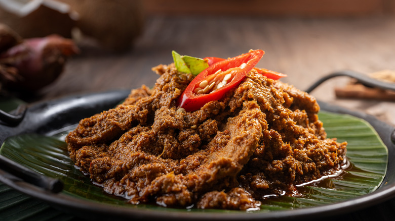 A plate of beef rendang garnished with sliced chile peppers