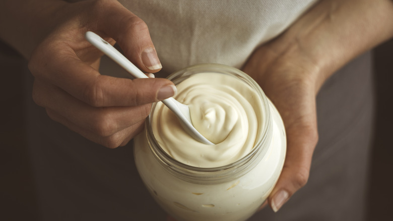 Person holding a jar of mayonnaise with a spoon