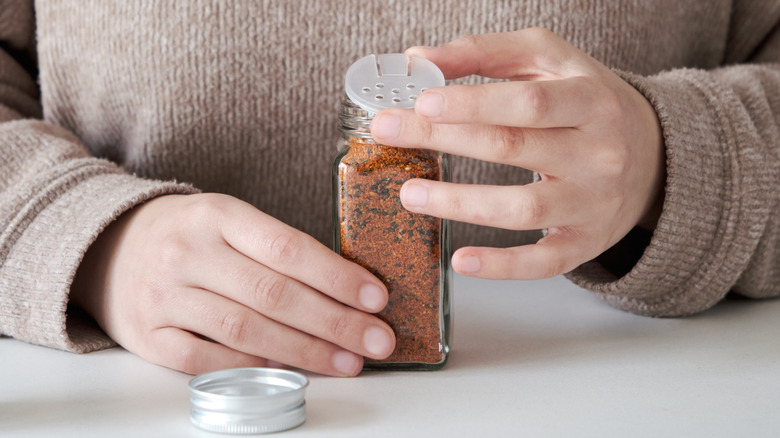 Close-up of a person's hands placing a sifter cap on a jar of shichimi togarashi